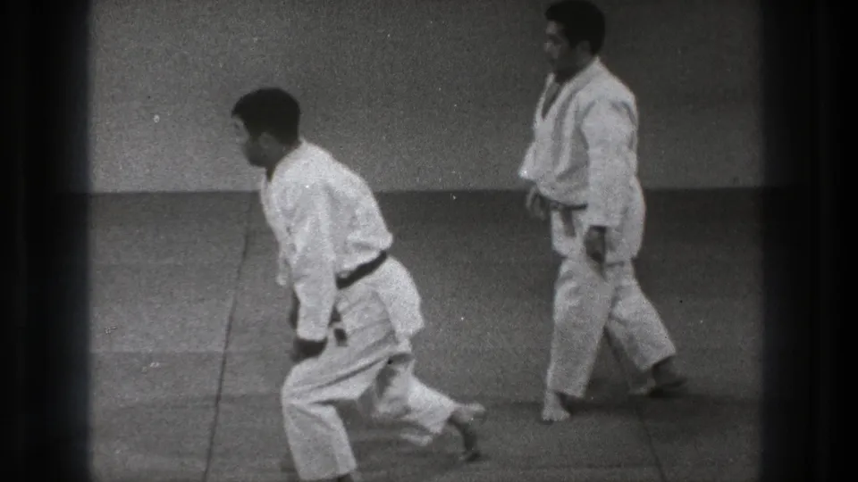 1971 Tokyo 8mm frame showing two martial arts practitioners in white gi on a matted practice floor.