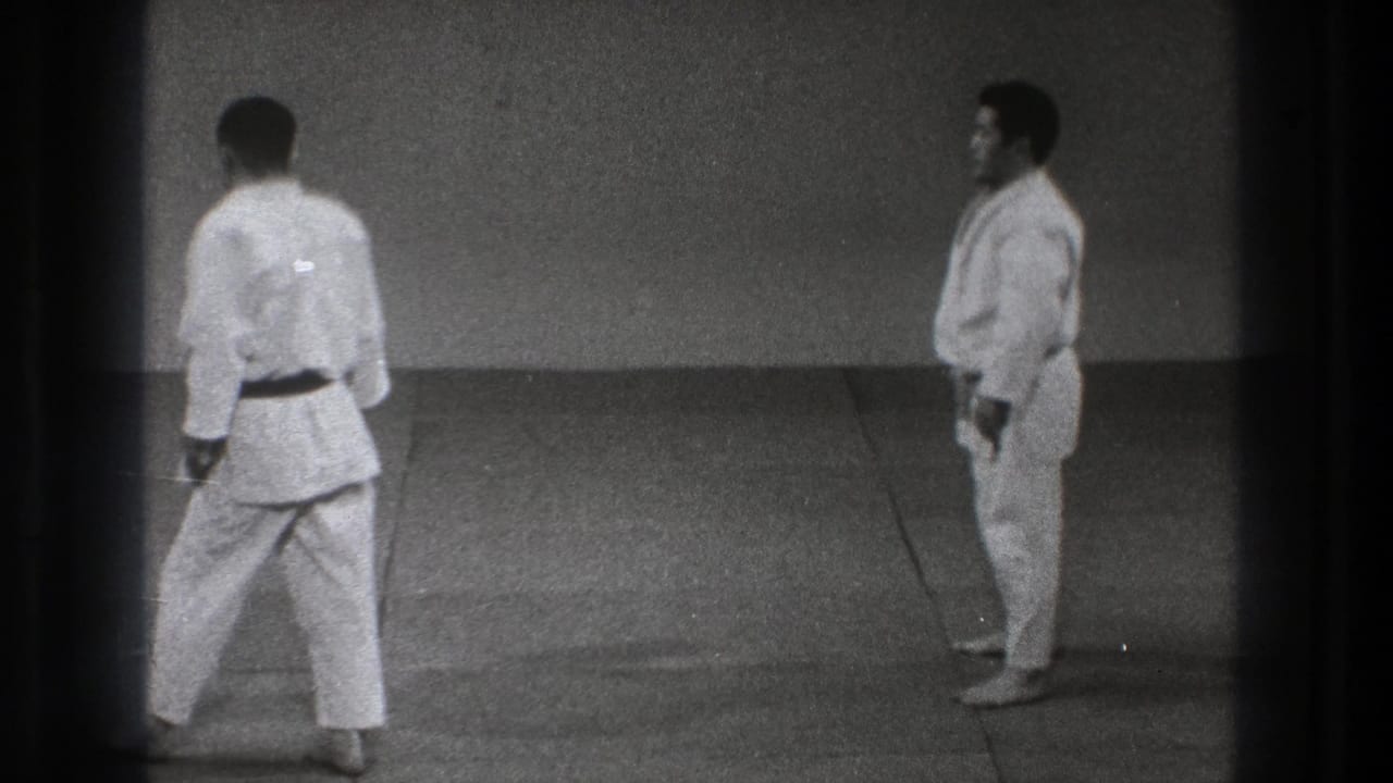 Two martial arts practitioners face off in a Tokyo practice setting, filmed on grainy 8mm in 1971.