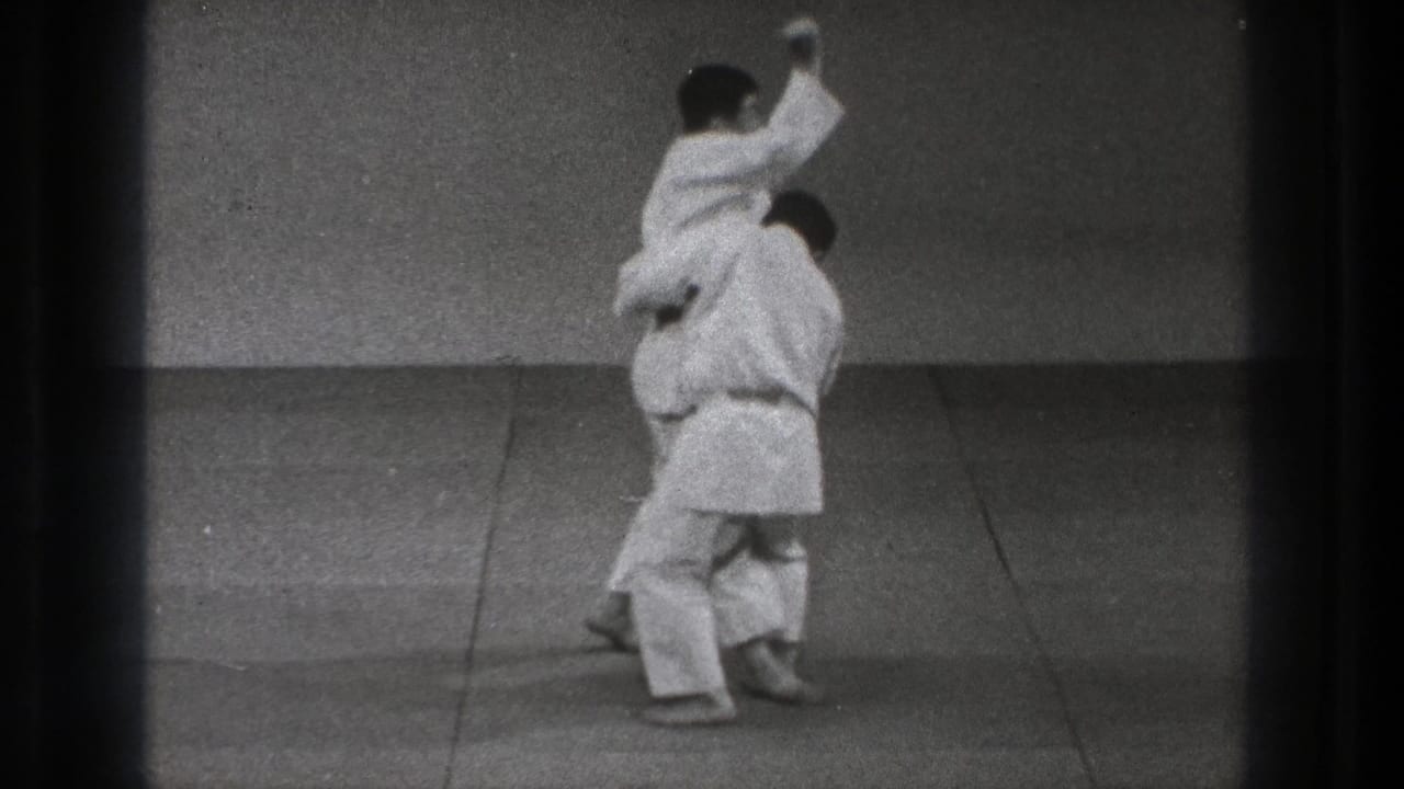 1971 Tokyo martial arts demonstration frame with one gi-clad practitioner raised over the defender during the technique.