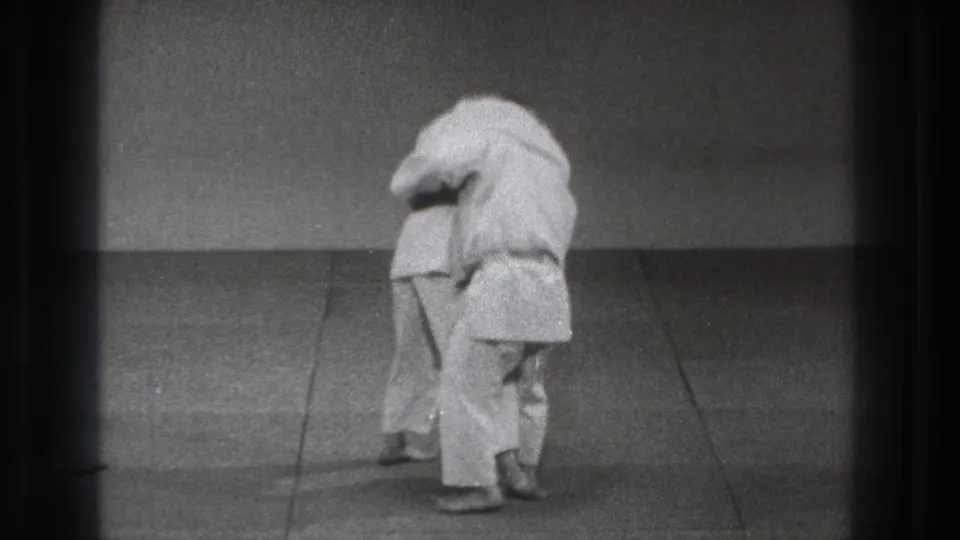 1971 Tokyo 8mm frame showing two martial arts practitioners in close contact during a grappling or throwing sequence.