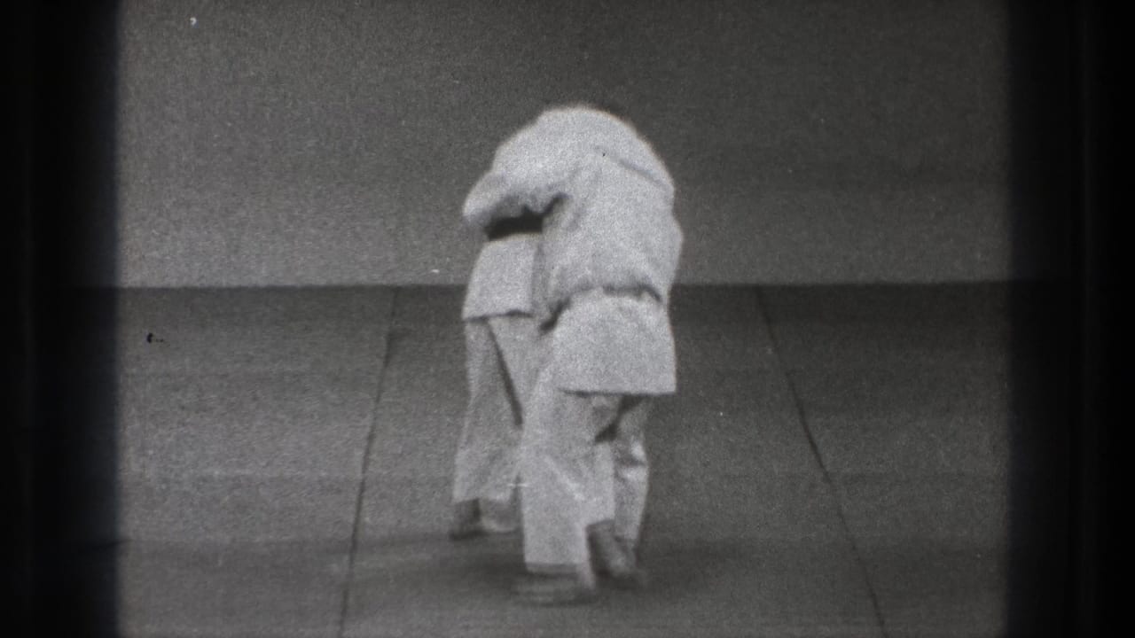 Late frame from the 1971 Tokyo martial arts clip showing the practitioners maintaining close grappling contact on the mat.