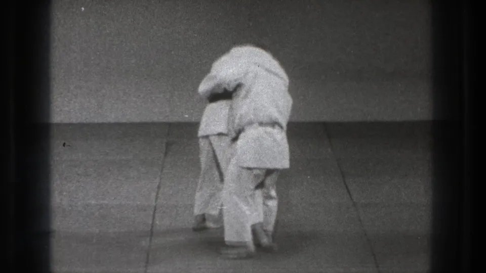 Late frame from the 1971 Tokyo martial arts clip showing the practitioners maintaining close grappling contact on the mat.