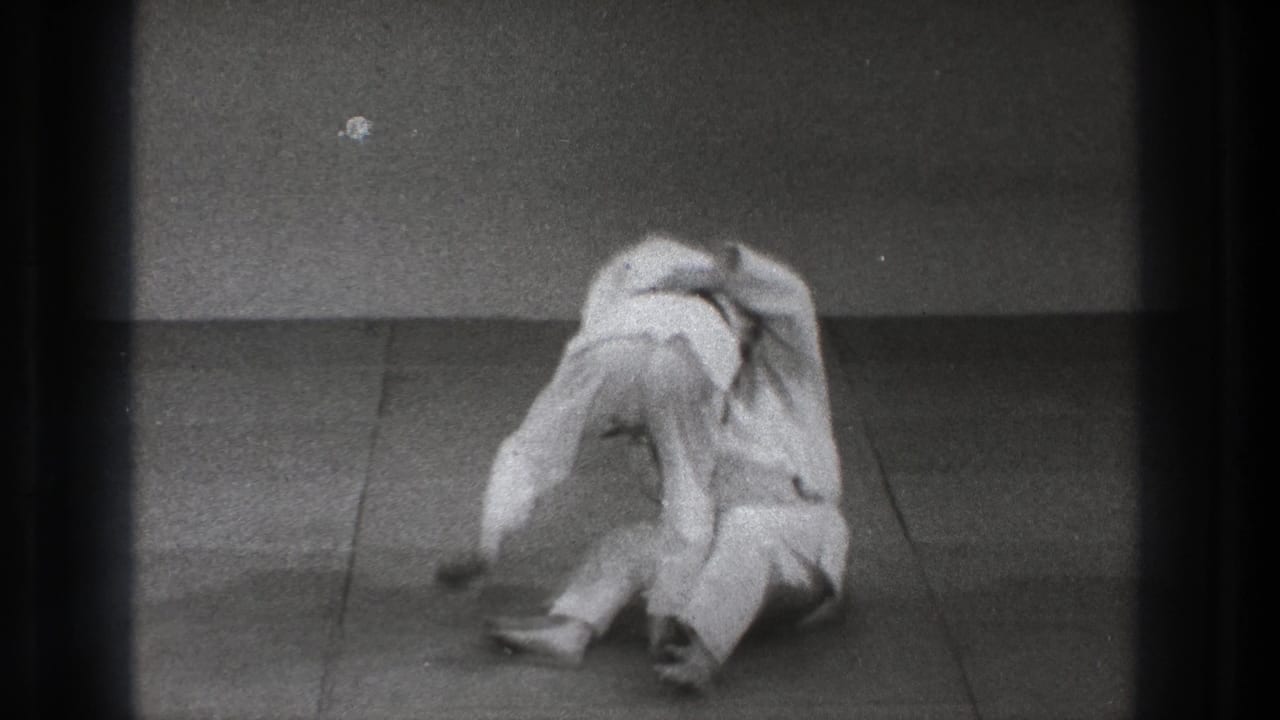 During the 1971 Tokyo training moment, both adults in gi drop close to the mat as the defensive throw develops.
