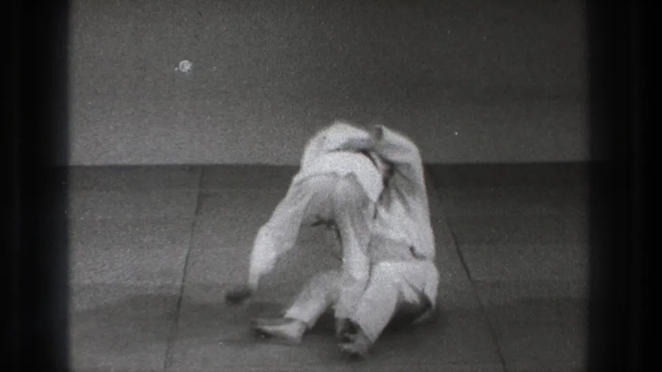 During the 1971 Tokyo training moment, both adults in gi drop close to the mat as the defensive throw develops.