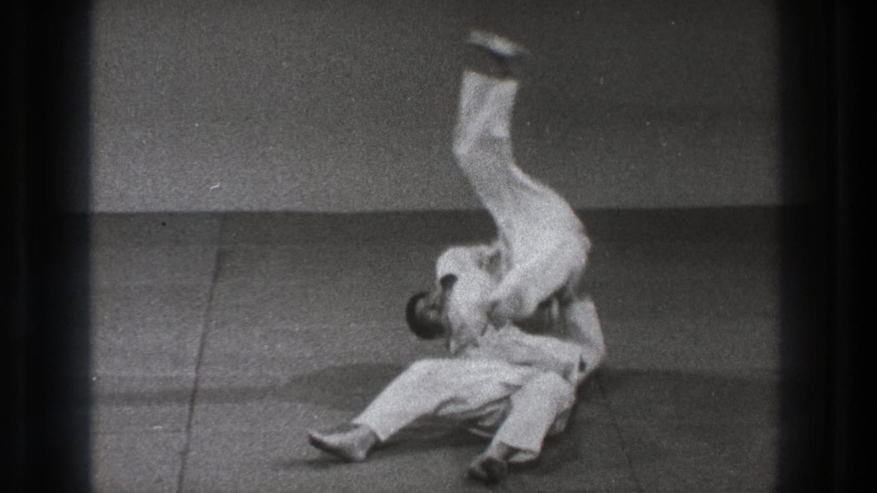 The throw reaches its peak as one adult in a white gi flips upside down over another practitioner on the Tokyo training mat.
