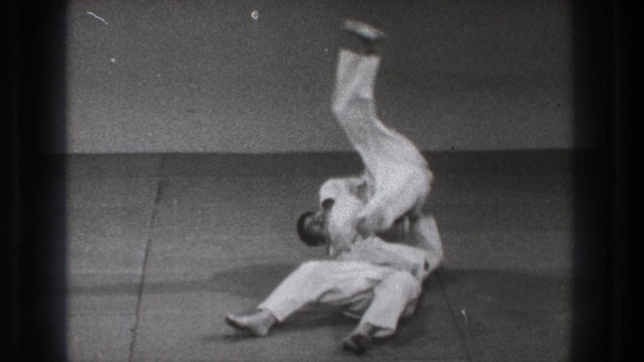 Two martial artists in white gi on a mat as one is lifted into a throw.