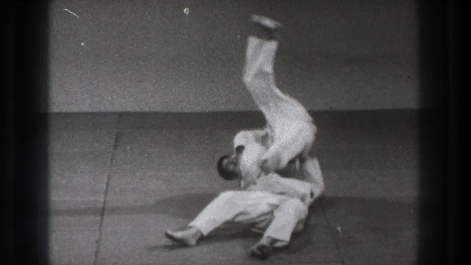 1971 Tokyo 8mm frame of two adult martial artists in white gi during a judo-style throw on indoor mats.