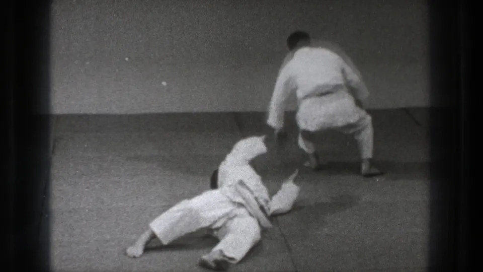 1971 Tokyo 8mm frame showing one practitioner down on the mat while another crouches after a judo movement.