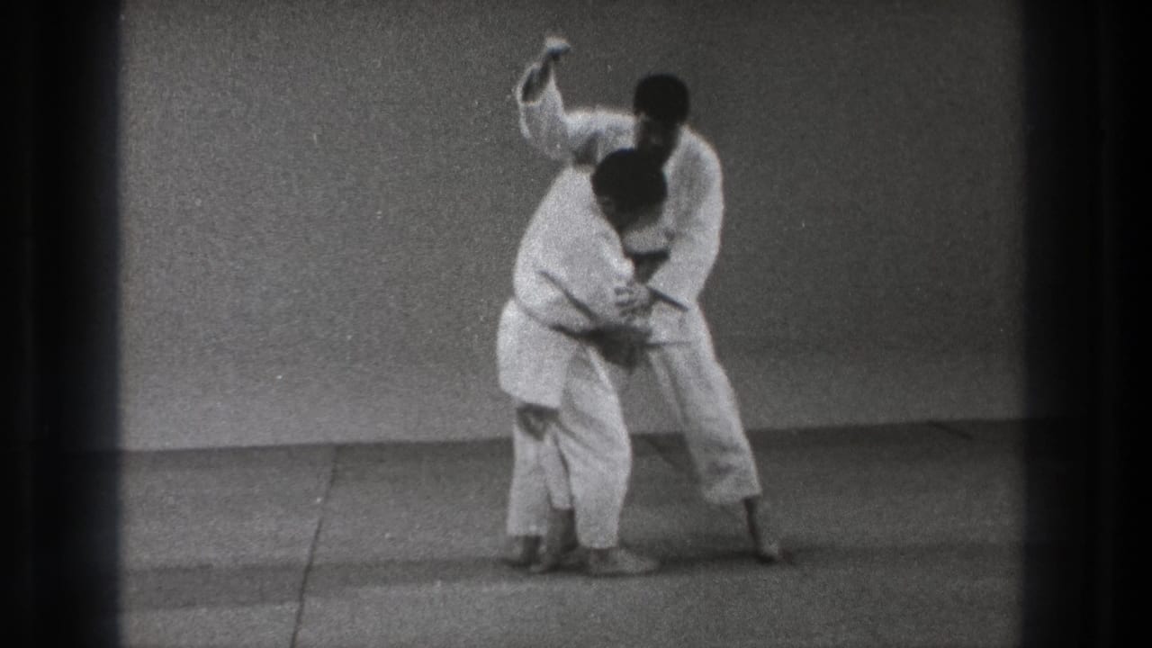 The Tokyo 1971 martial arts demonstration continues as one practitioner controls the other's upper body on the mat.