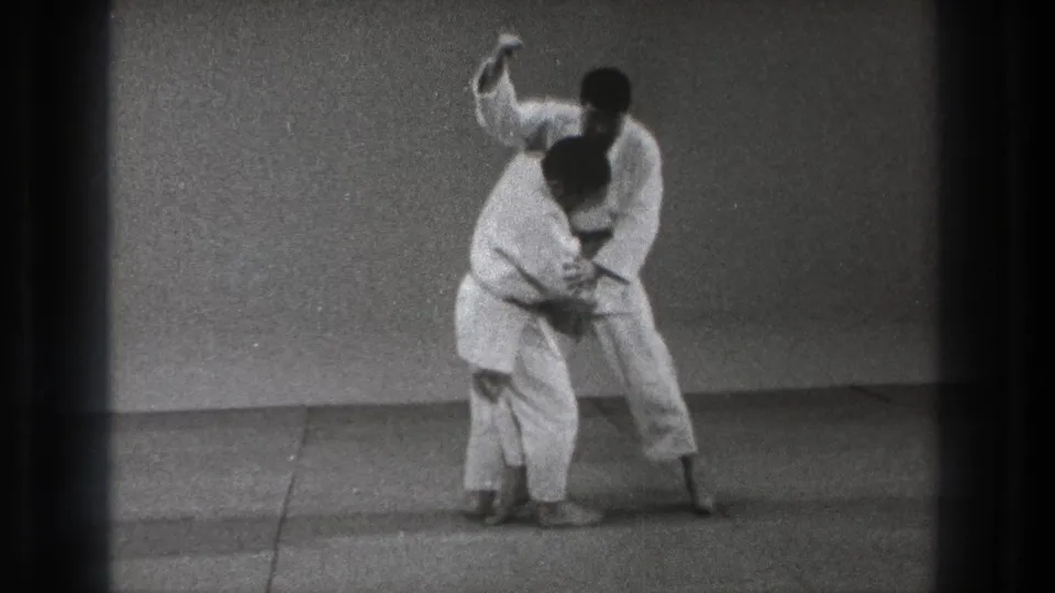 The Tokyo 1971 martial arts demonstration continues as one practitioner controls the other's upper body on the mat.