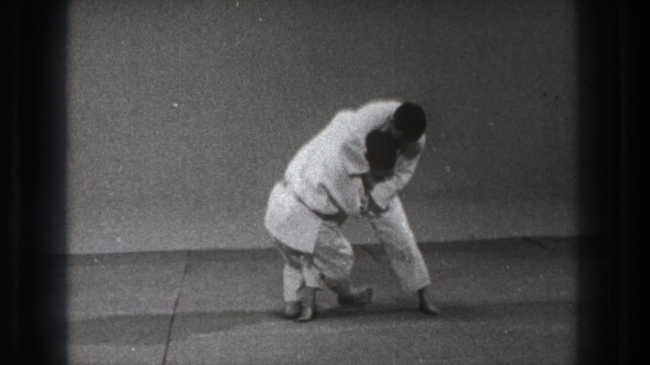 Two martial artists maintain a low stance while one controls the other's arm or sleeve.