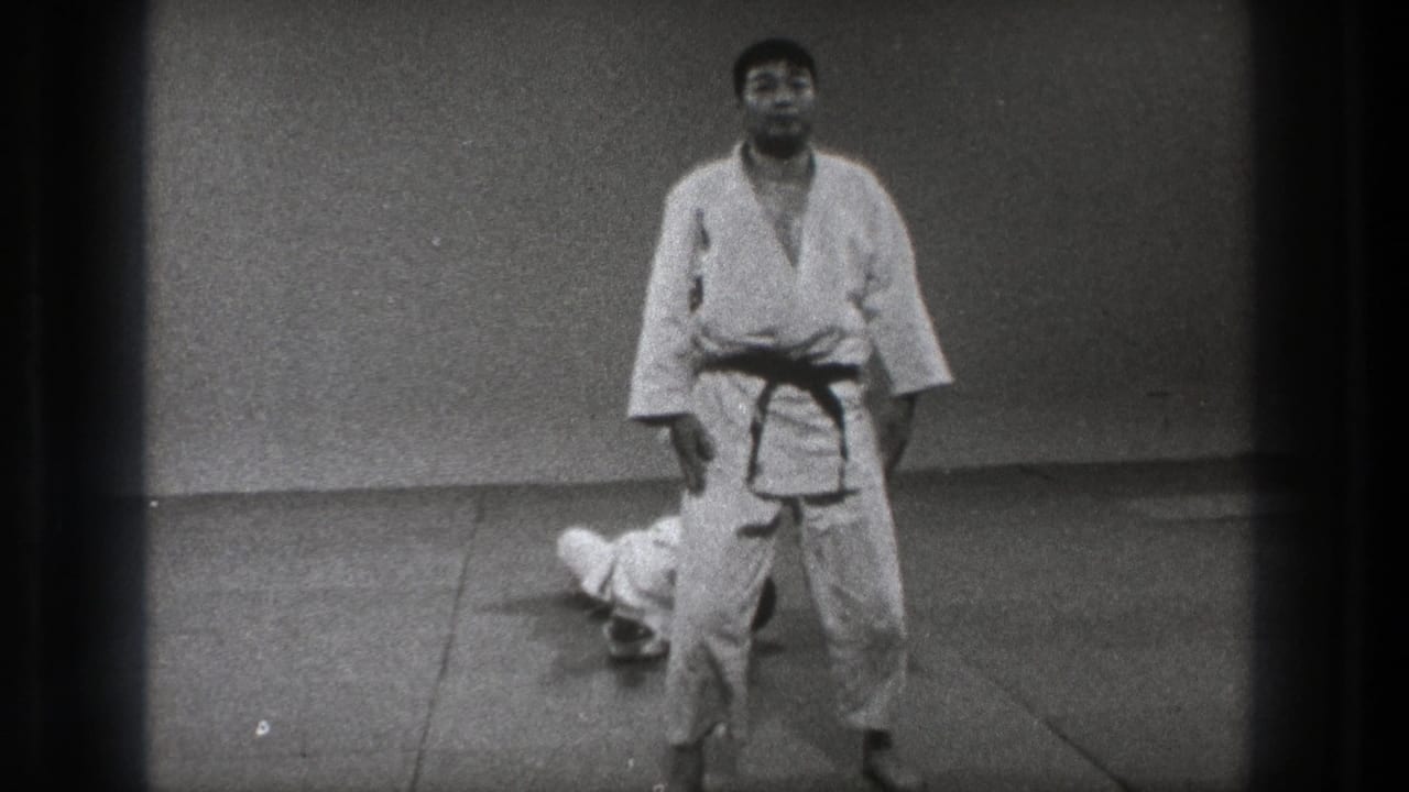1971 Tokyo frame with one martial arts practitioner standing in a formal posture as another remains on the indoor mat.