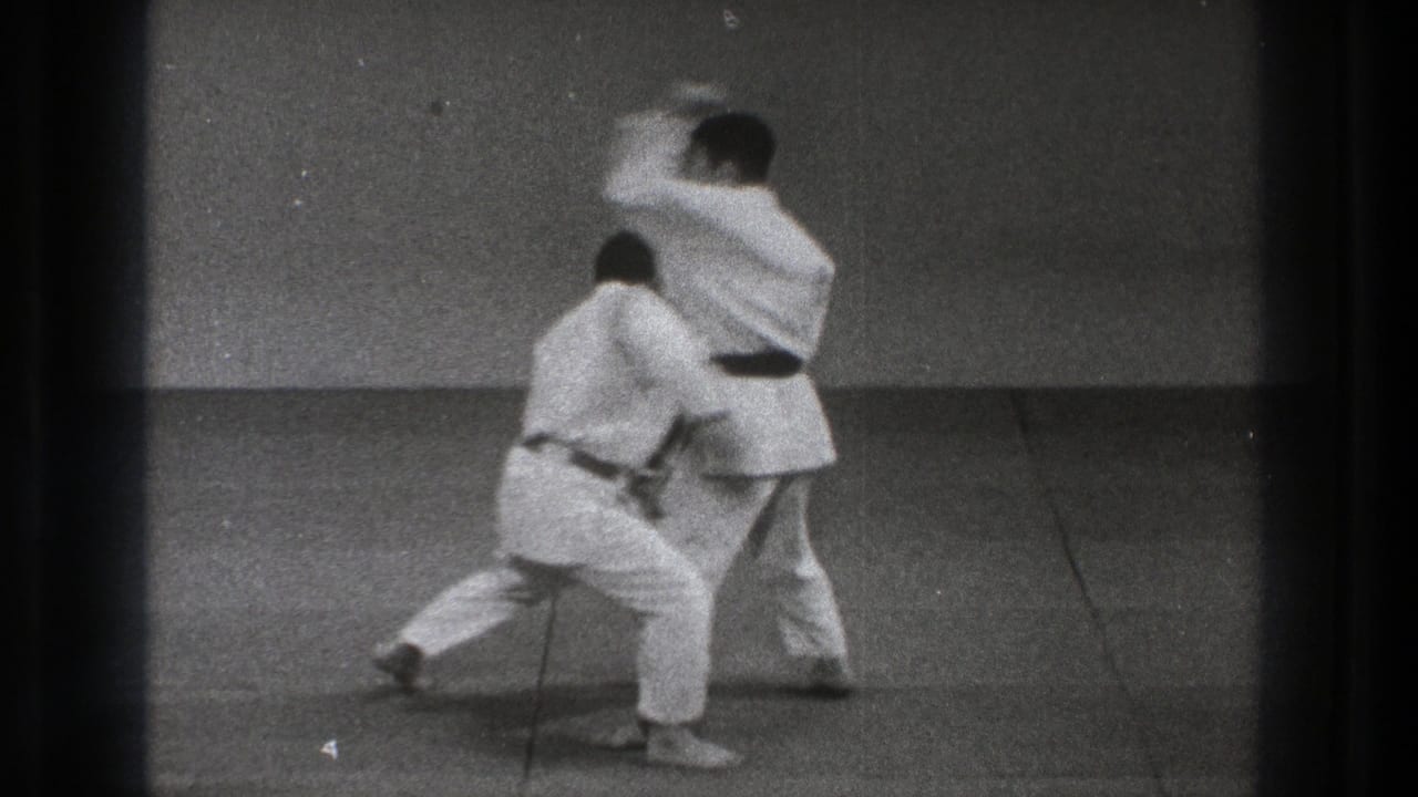 1971 Tokyo frame showing two men in white uniforms mid-motion during an indoor martial arts throwing drill.