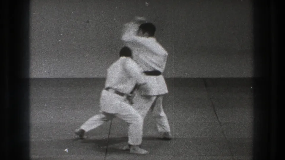 1971 Tokyo frame showing two men in white uniforms mid-motion during an indoor martial arts throwing drill.
