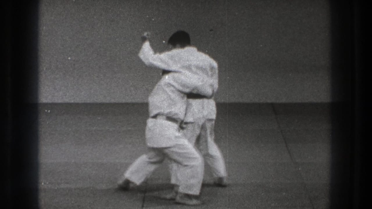 Two martial artists in white gi grip each other on a mat.