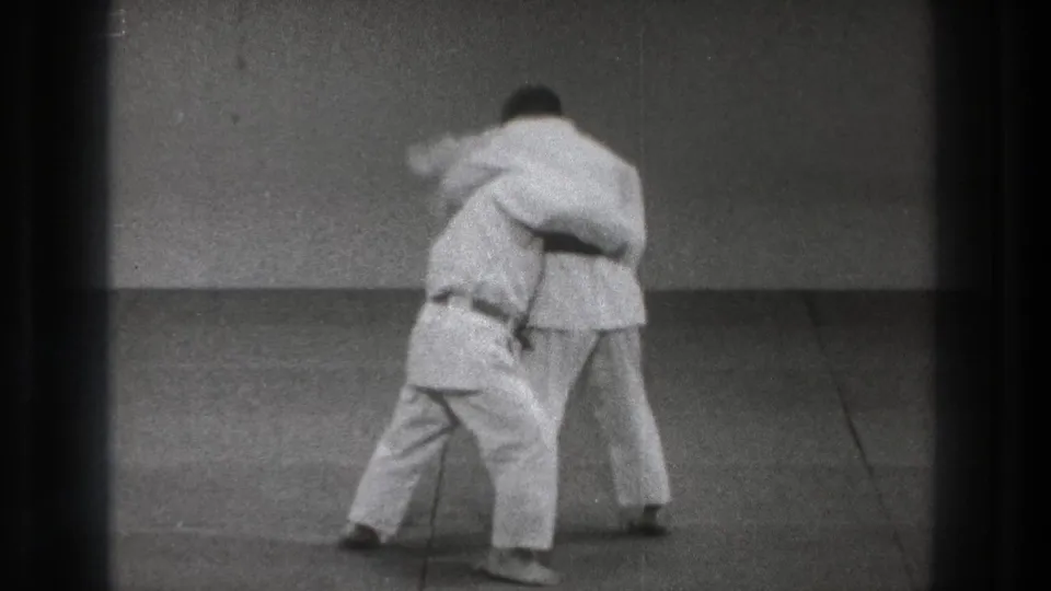 A judo practitioner in a white gi steps inside and lowers his stance while maintaining a body grip during practice in Tokyo, 1971.