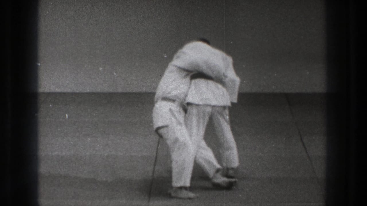 Near the end of the 1971 Tokyo judo sequence, one practitioner drops low as the other controls the grip during the throw practice.