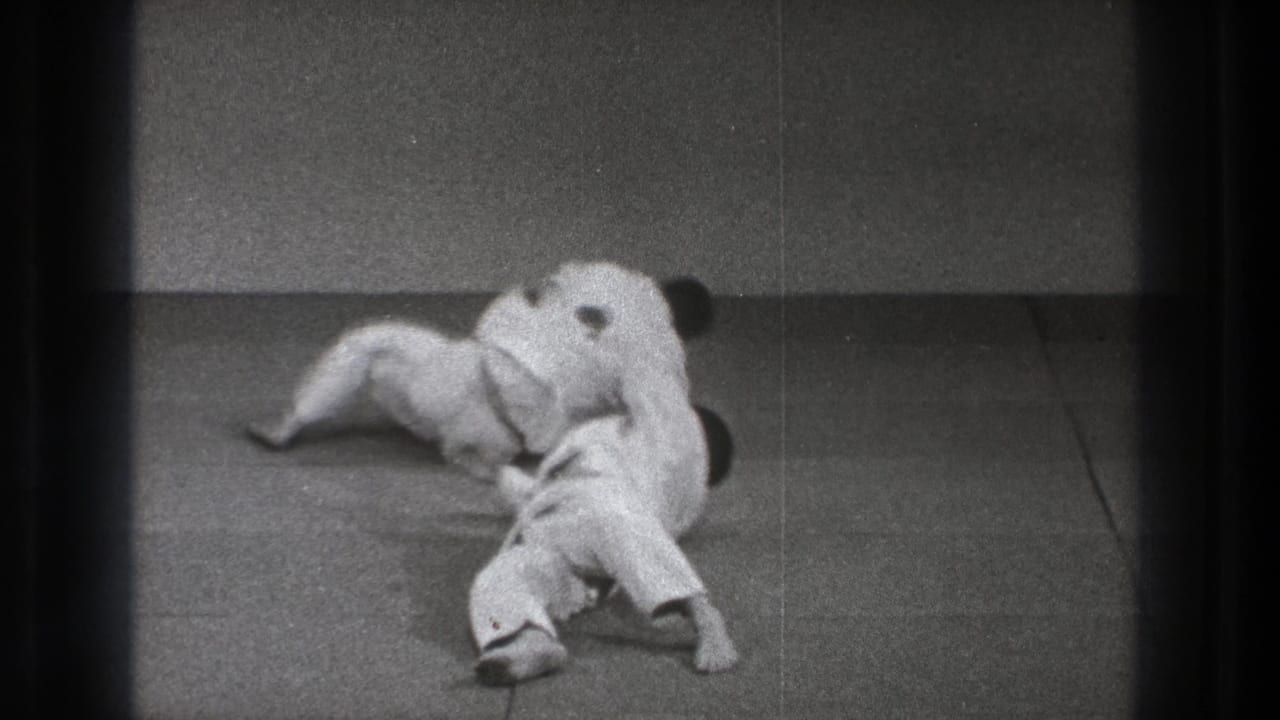 The throw resolves with both practitioners down on the mat, their white gi and limbs overlapping in the final landing position.