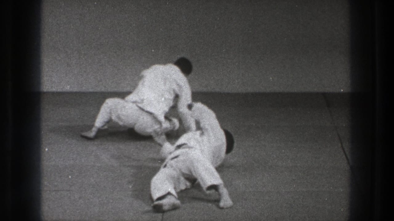 Two men in white martial arts uniforms grapple on a mat.