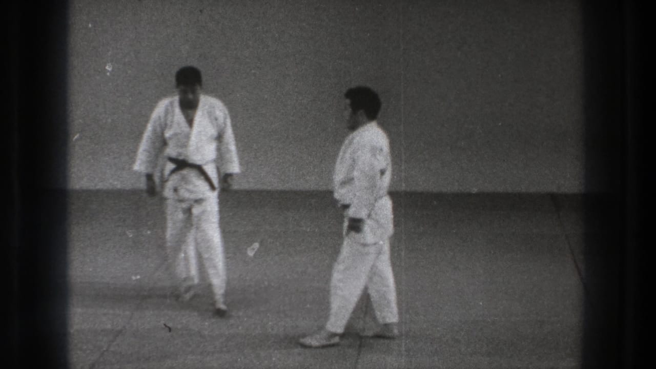 Black-and-white 8mm frame of two karate practitioners in Tokyo, 1971, standing close on a dojo mat.