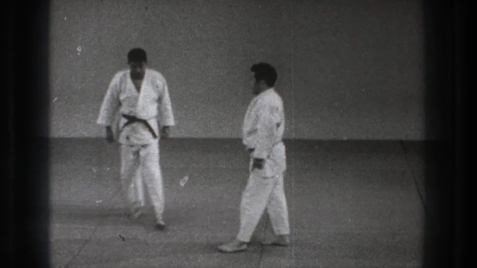 Black-and-white 8mm frame of two karate practitioners in Tokyo, 1971, standing close on a dojo mat.