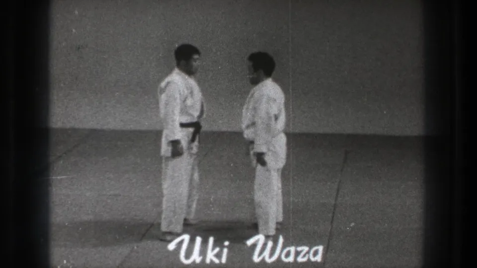 The two practitioners face each other on the mat as a handwritten Uki Waza title appears over the 8mm frame.