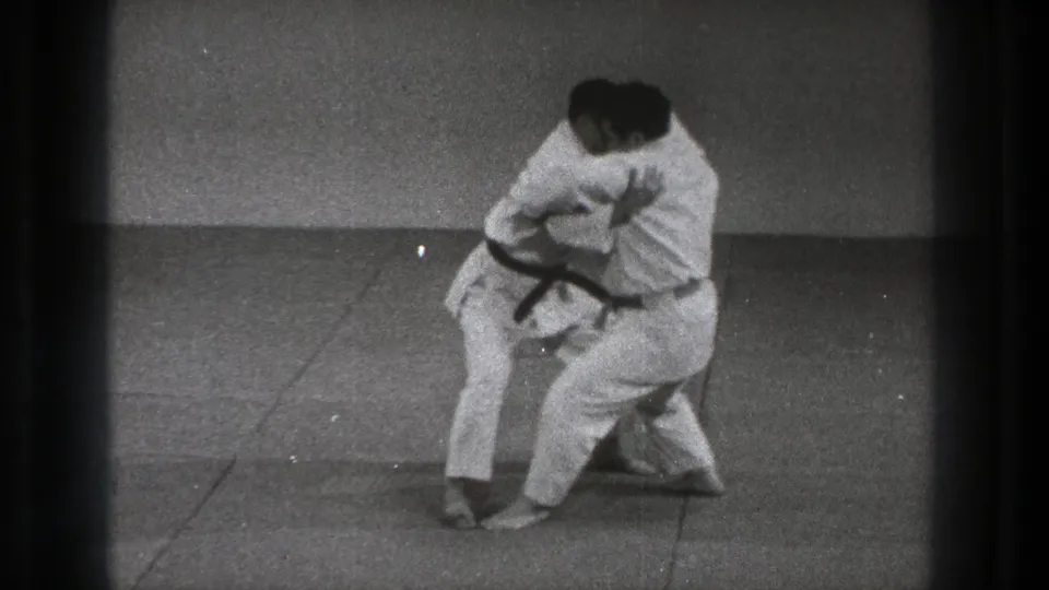 A 1971 Tokyo martial arts drill shows one man lowering his stance while maintaining a hold on his partner.