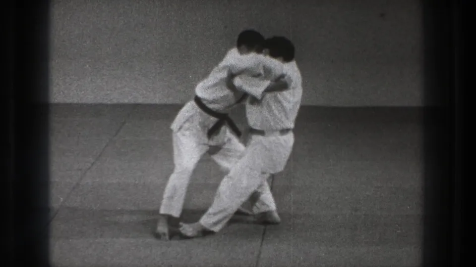 Near the end of the 1971 Tokyo clip, two gi-clad men shift through a controlled grappling motion on mats.