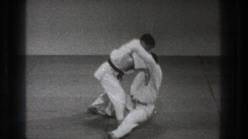 The throw finishes with one man low on the mat and the other leaning above him in black-and-white 8mm Tokyo 1971 footage.