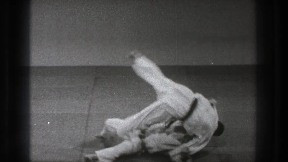 In supported 1971 Tokyo 8mm footage, two adult judo practitioners in white uniforms are mid-throw on an indoor mat.
