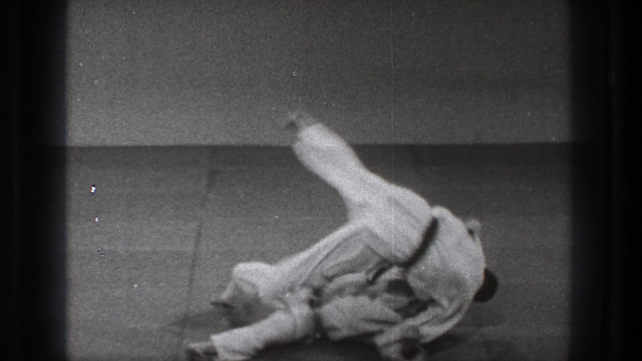 Two adult martial artists in white judogi roll on a mat in a simple Tokyo training-room scene from 1971 footage.