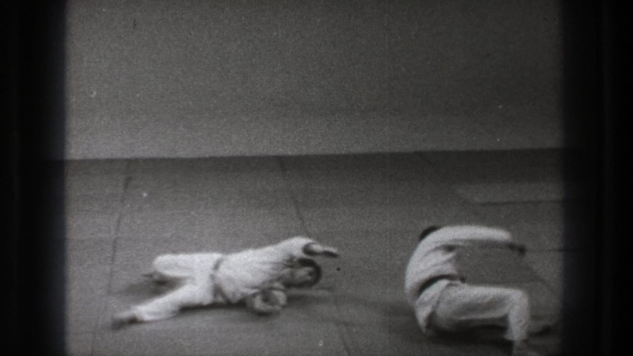 A 1971 Tokyo judo practice frame shows one adult on the mat and another completing a roll in white training clothes.