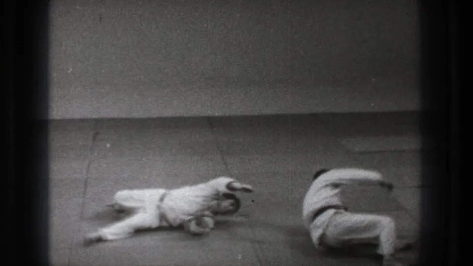 A 1971 Tokyo judo practice frame shows one adult on the mat and another completing a roll in white training clothes.