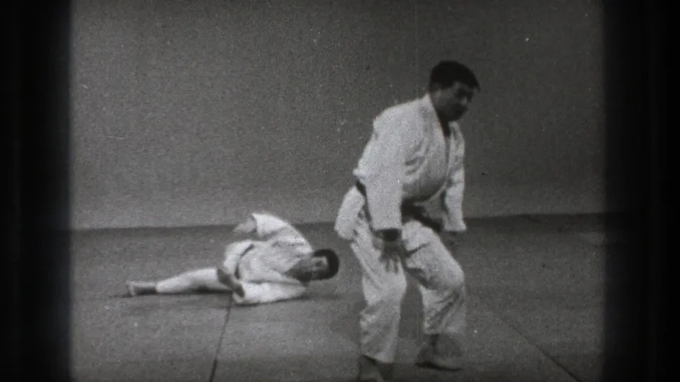1971 Tokyo 8mm frame showing two men in martial arts gi after a throw on a plain indoor mat.
