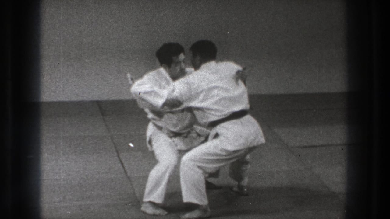 Black-and-white 8mm frame of two martial arts practitioners in close contact during a grappling technique.
