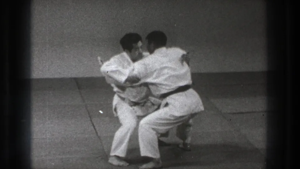 Black-and-white 8mm frame of two martial arts practitioners in close contact during a grappling technique.