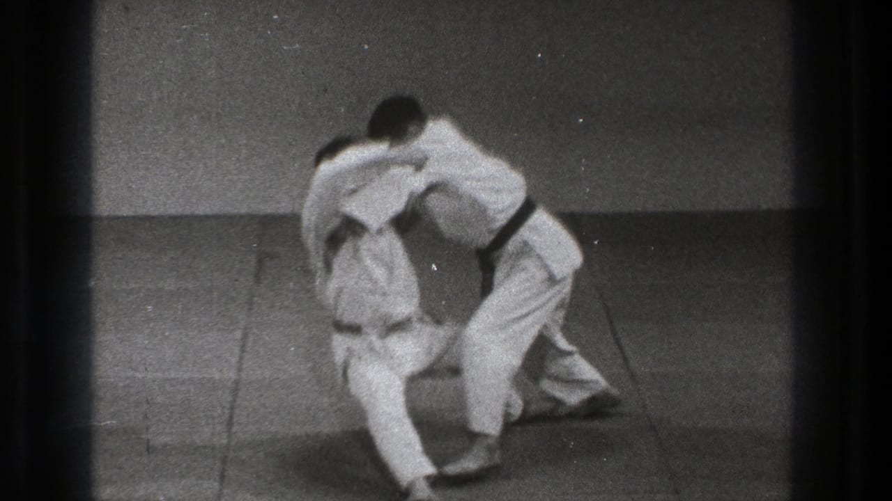 Two men in white martial arts uniforms grapple on a mat.