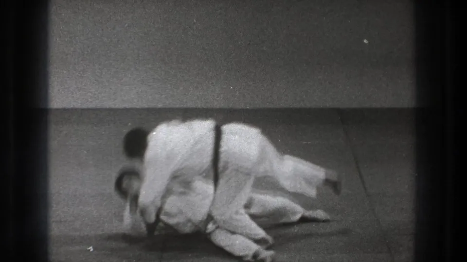 One uniformed martial artist takes his opponent down on a mat, with both bodies low during the throw sequence.