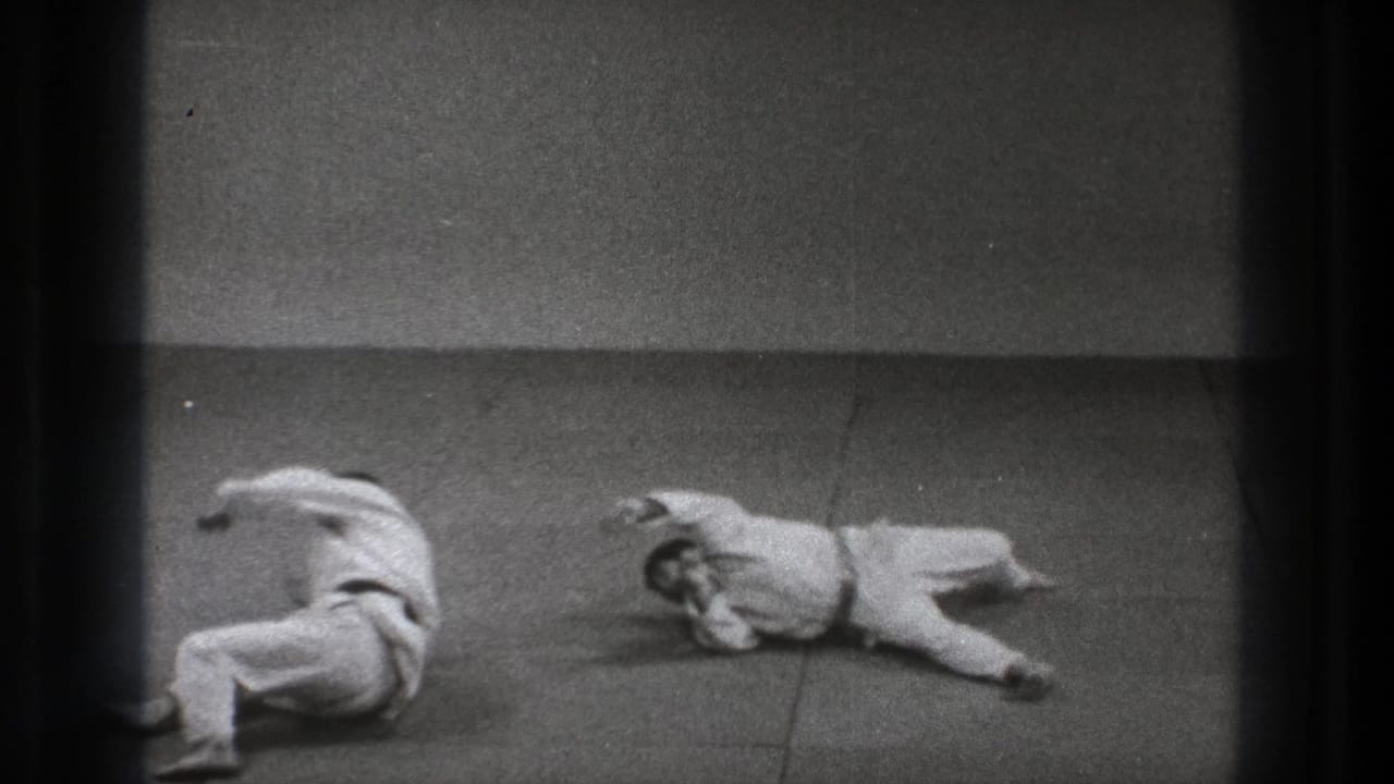 After the throw, the two uniformed men are separated on the mat, one curled near the center and the other lying to the side.