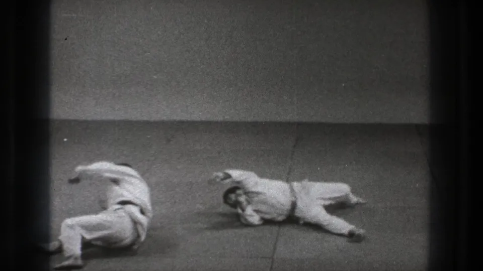 After the throw, the two uniformed men are separated on the mat, one curled near the center and the other lying to the side.