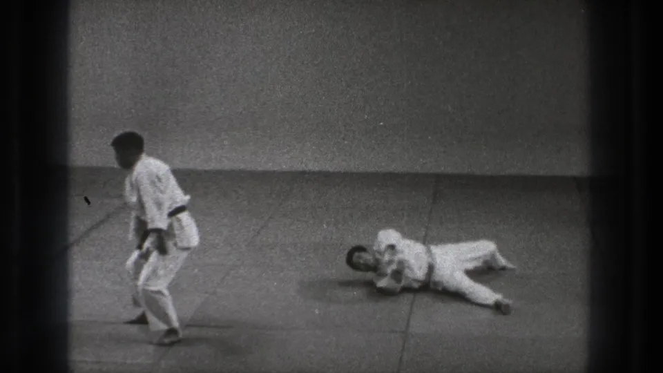 In metadata-supported Tokyo 1971 footage, two men in white gi practice on a mat as one remains standing and the other lies after a throw.