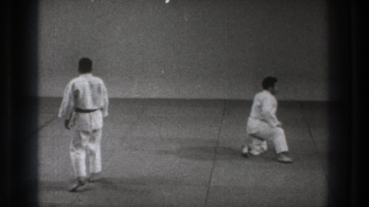 The 1971 Tokyo training footage shows one martial artist seen from behind while the other kneels, continuing the recovery sequence.