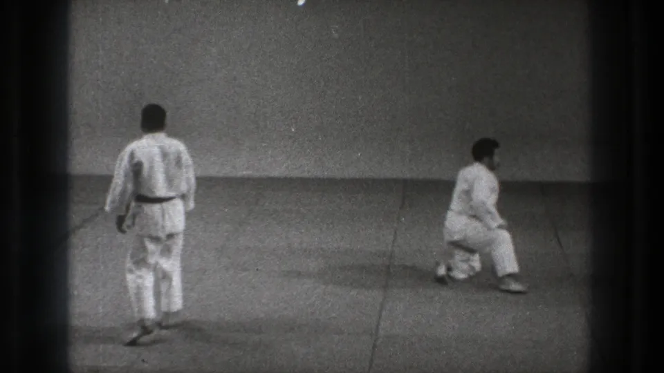 The 1971 Tokyo training footage shows one martial artist seen from behind while the other kneels, continuing the recovery sequence.