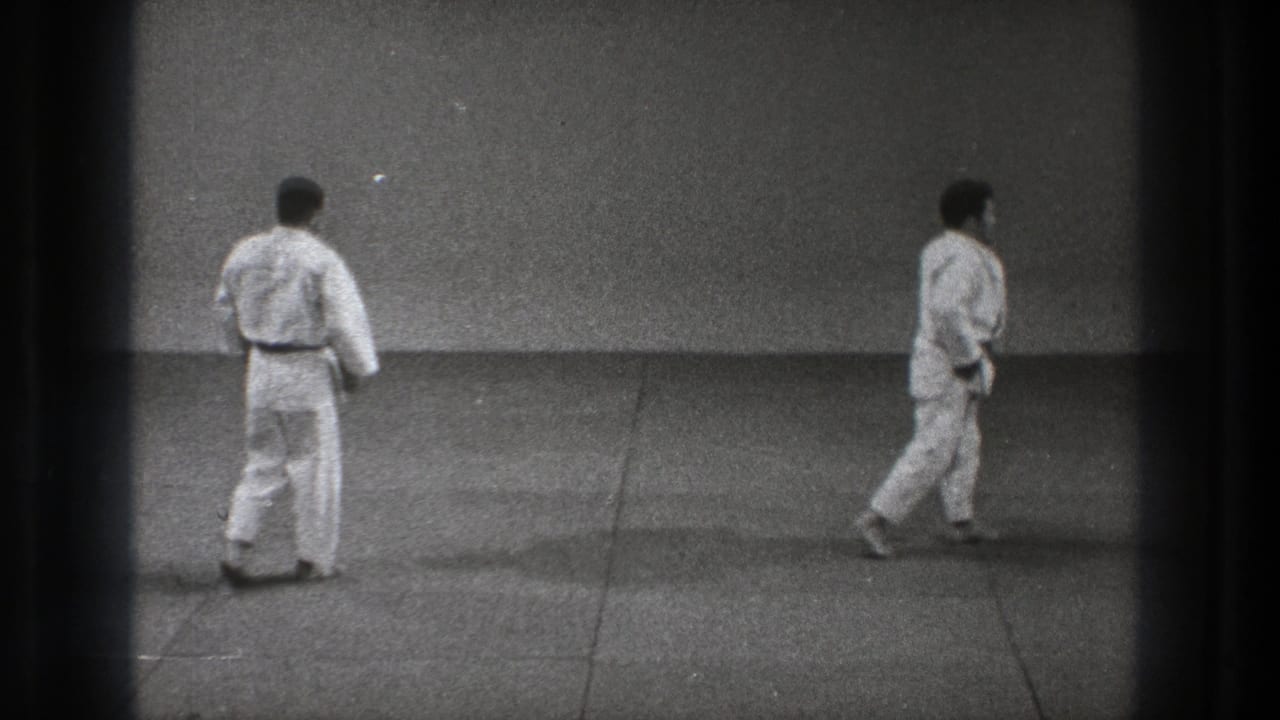 Two men in white karate uniforms stand on a mat, seen from behind and side view.