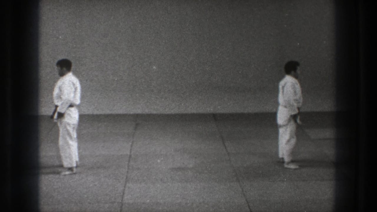 Two karate practitioners in white uniforms face toward the center of a mat, captured in grainy black-and-white 8mm footage from Tokyo, 1971.