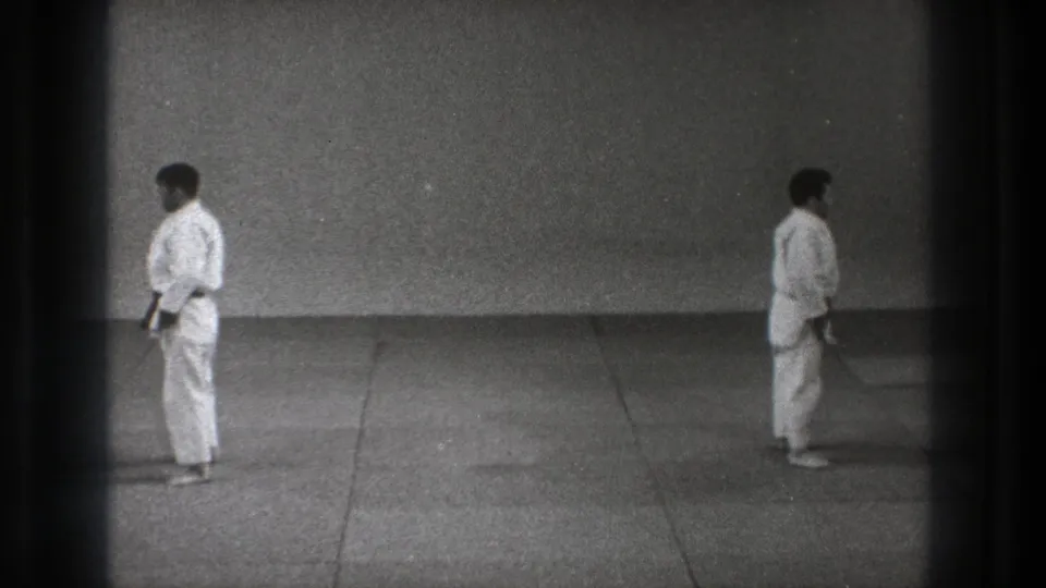 Two karate practitioners in white uniforms face toward the center of a mat, captured in grainy black-and-white 8mm footage from Tokyo, 1971.