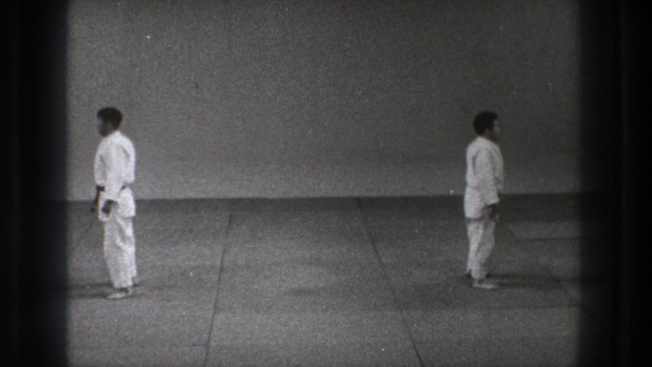 A black-and-white 8mm frame from Tokyo, 1971 shows two men in white karate uniforms standing opposite each other on a simple mat floor.