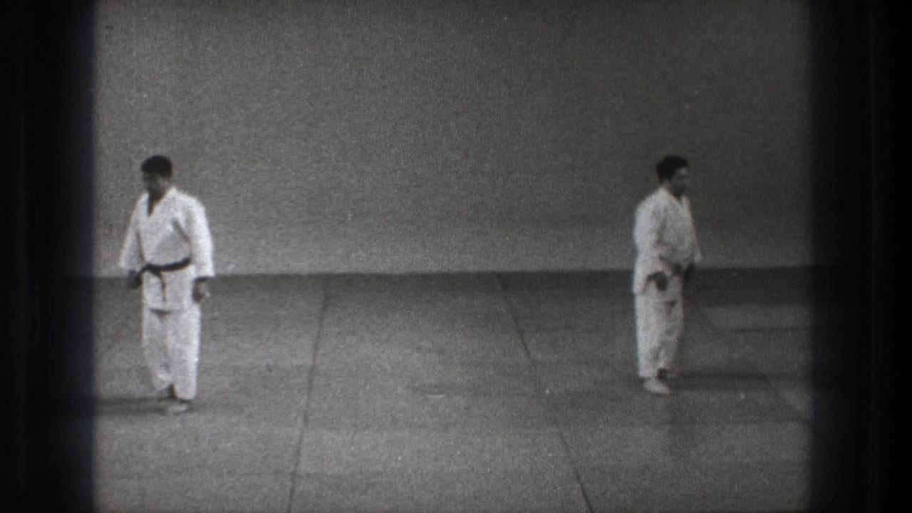 Two men in white martial arts uniforms stand apart on a mat.