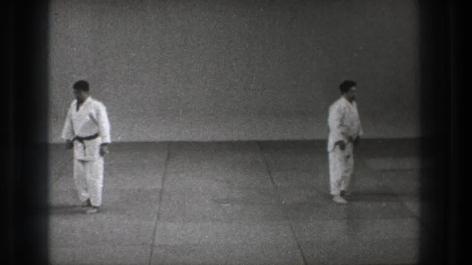 In 1971 Tokyo footage, two men in white gi face each other across a simple mat in a sparse training room.