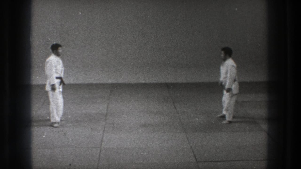 A wide 8mm frame shows two martial arts practitioners in gi maintaining distance on the mat in Tokyo, 1971.